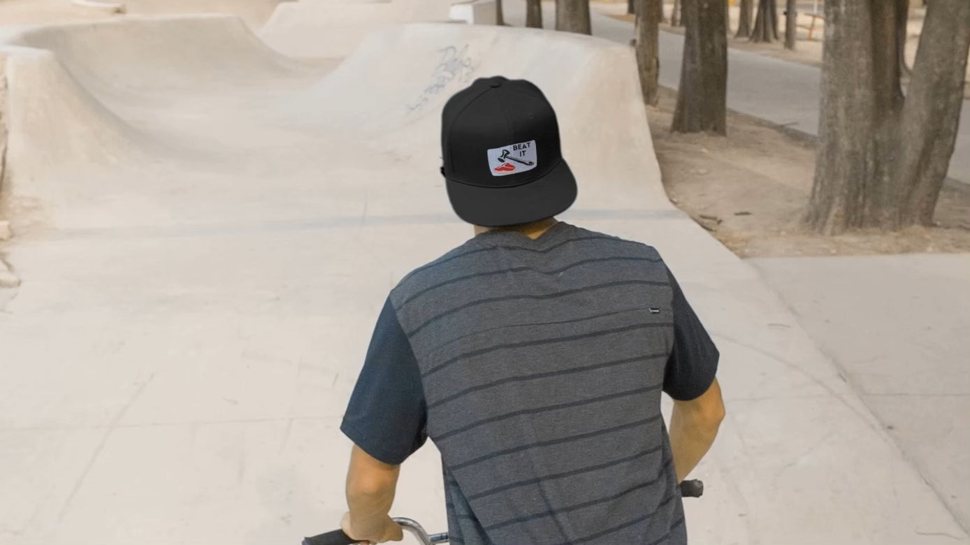 Load video: video of a man riding a bike with a beat it black hat from ballsy hats.